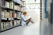 © Westend61 - Student in a university library sitting on floor reading book