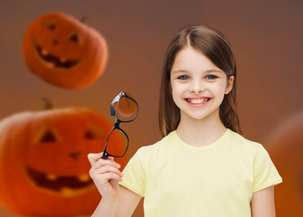 Wall Mural - smiling girl in glasses over pumpkins background