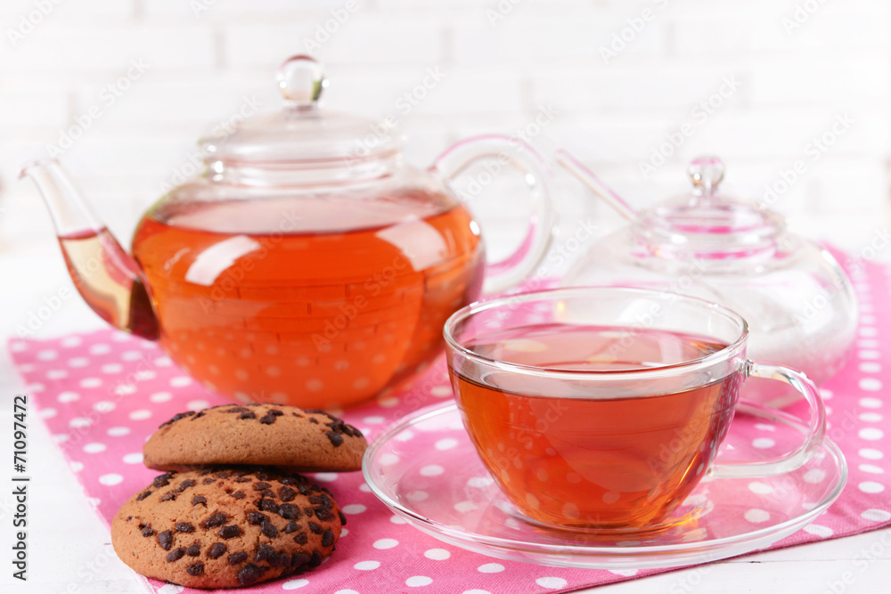 Teapot and cup of tea on table on brick wall background