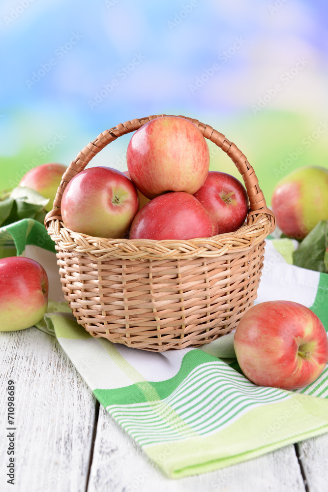 Sweet apples in wicker basket on table on bright background