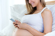 © nenetus - Pregnant woman using her mobile phone on sofa.