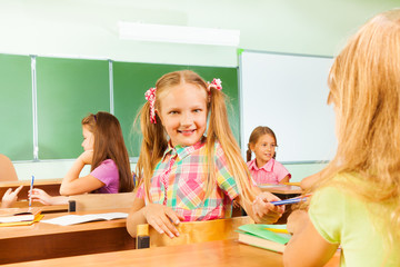 Wall Mural - Smiling girls turned to classmate giving pencil