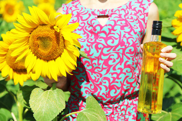 Canvas Print - Young woman holding bottle of oil and sunflower in field