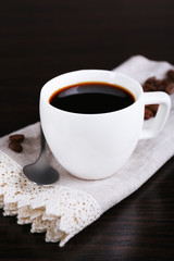 Cup of coffee and coffee beans on napkin on dark background