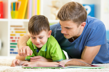 Poster - child and his father read a book on floor at home