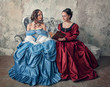 Two beautiful women in medieval dresses on the sofa reading book