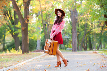 Beautiful brunette girl with suitcase in the park.