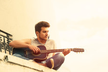 Young Guitarist Sitting On Parapet, View From Below