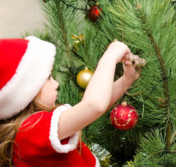 Little girl in santa hat decorating the christmas tree