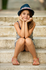 Cute young girl with hat sitting on stairs in park