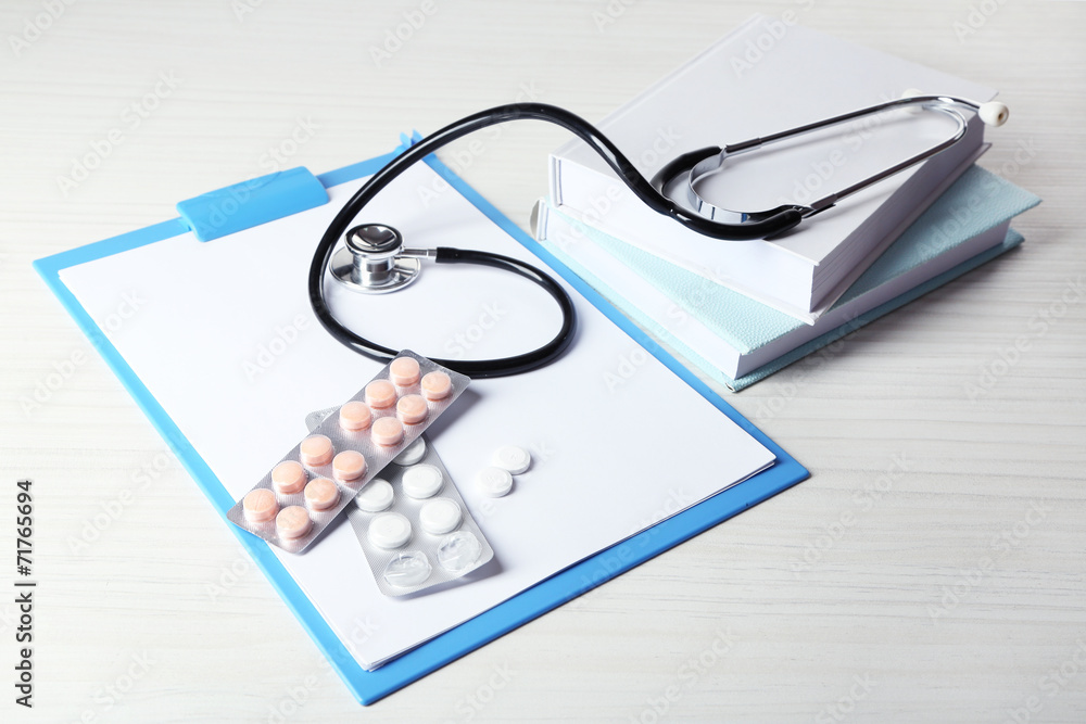 Medical stethoscope with books and folder on wooden table