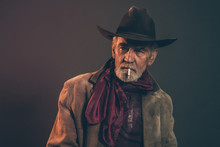 Old Rough Western Cowboy With Gray Beard And Brown Hat Smoking A