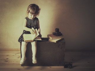 little girl reading a book on the old suitcase