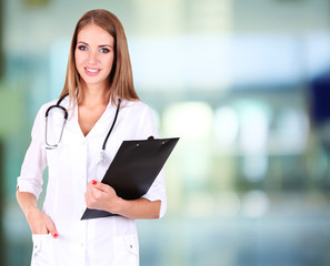 Poster - Young beautiful doctor holding folder on hospital background