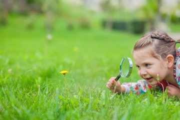 little cute girl with magnifying glass examining flower