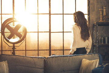 Wall Mural - Young woman looking in window in loft apartment. rear view