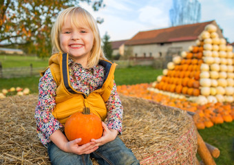 Wall Mural - Portrait of happy child sitting on haystack with pumpkin