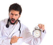 Surprised Doctor Holding A Clock Over White Background
