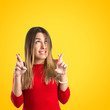 Young girl crossing his fingers over yellow background