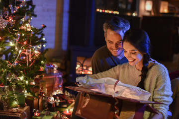 Wall Mural - Handsome couple opening a gift in front of the Christmas tree li