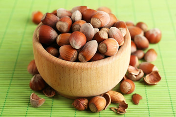Wall Mural - Hazelnuts in wooden bowl on bamboo mat background