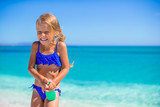 Fototapeta  - Little happy girl with suntan lotion bottle during beach
