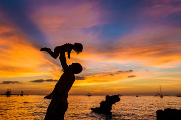 silhouettes of father and child on sunset sea background