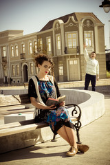 girl reading book on bench in town while the man in the backgrou