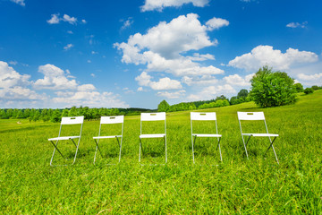 Five white chairs stand in a row on green grass