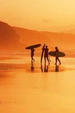 Surfers On The Shore At Sunset