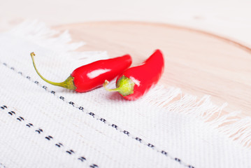 Two chili peppers on a cutting board with a napkin on a light wo