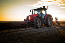 Farmer Plowing Stubble Field With Red Tractor At Sunset