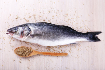 Fresh fish and salt in spoon on wooden background