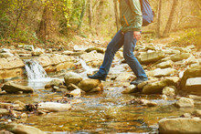 Hiker Man Crossing A River On Stones, View Of Legs