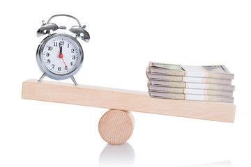 Alarmclock And Stacked Dollar Bundles Balancing On Seesaw