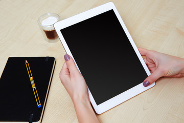 Girl hands holding a tablet pc with blank screen, wooden desk