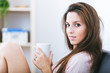 © photopitu - Smiling young woman on sofa with a cup of coffee at home