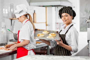 Happy Chef Holding Small Pizzas On Tray In Kitchen