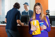 © Tyler Olson - Smiling Woman Holding Snacks While Man Buying Movie Tickets
