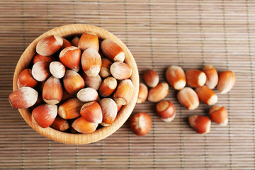 Wall Mural - Hazelnuts in wooden bowl on bamboo mat background