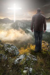 Wall Mural - Man on top of the mountain looking at Christian Cross at sunrise