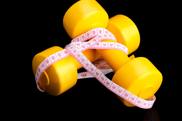 two yellow dumbbells and tape measure lying on a black backgroun