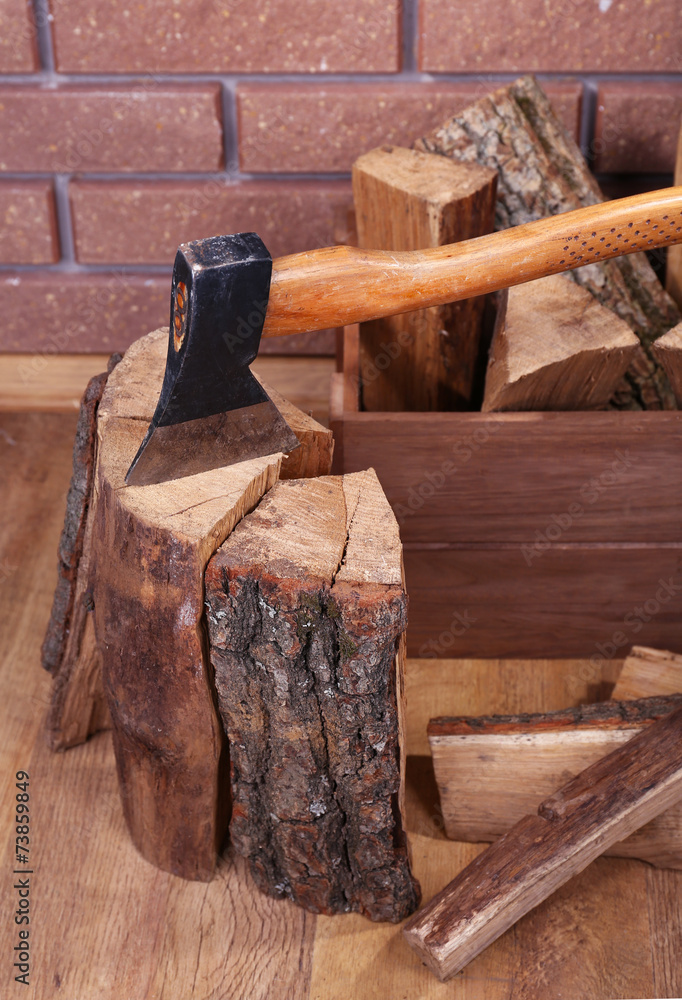 Box of firewood and axe on floor on brick background