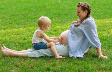 Pregnant woman and her son have a rest on the green grass