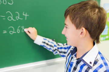 little smiling schoolboy writing on chalk board
