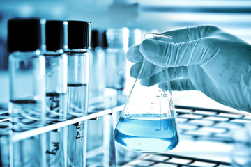 Wall Mural - hand of scientist holding flask with lab glassware in chemical laboratory background, science labora