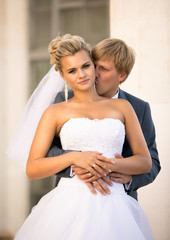 Wall Mural - young groom hugging blonde bride from back on street