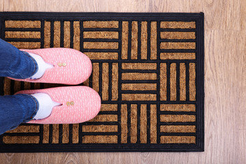 Wall Mural - Girl in home slippers on brown carpet on floor close-up