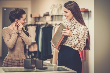 Young woman choosing jewellery with shop assistant  help