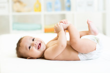 Baby Lying On White Bed And Holding Legs